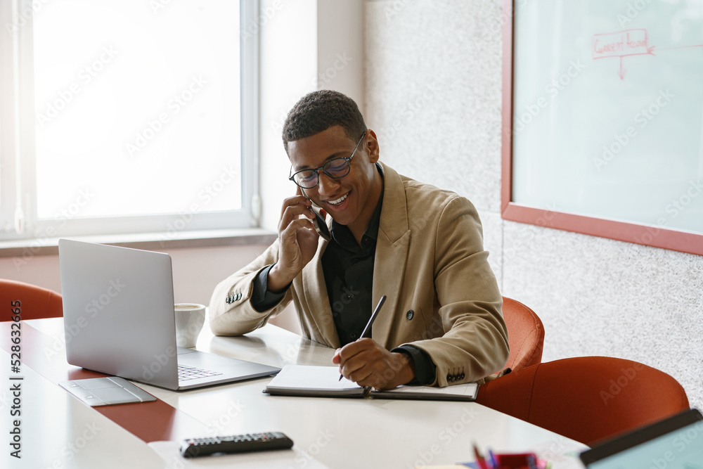 Smiling african businessman talking phone sitting in cozy coworking