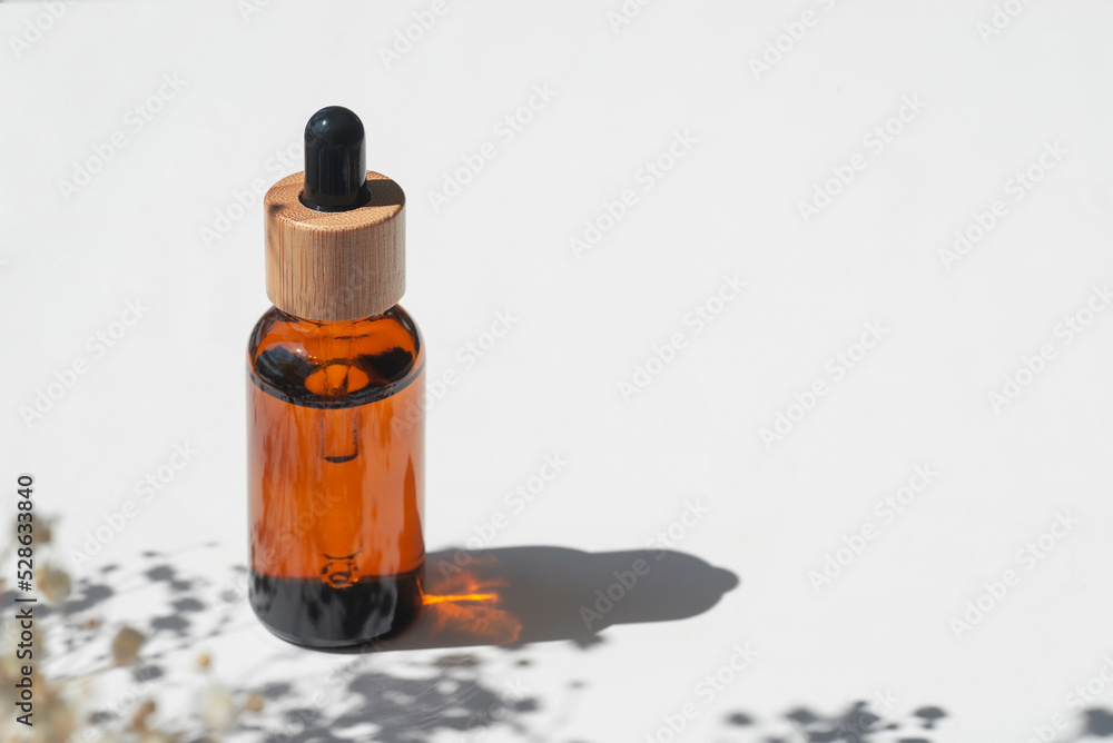 Amber bottle with cap with serum or essential oil with flowers shadows. White background with daylight. Beauty concept for face and body care. Soothing CBD oil Amber bottle with cap with serum or essential oil with flowers shadows. White background with daylight. Beauty concept for face and body care. Soothing CBD oil