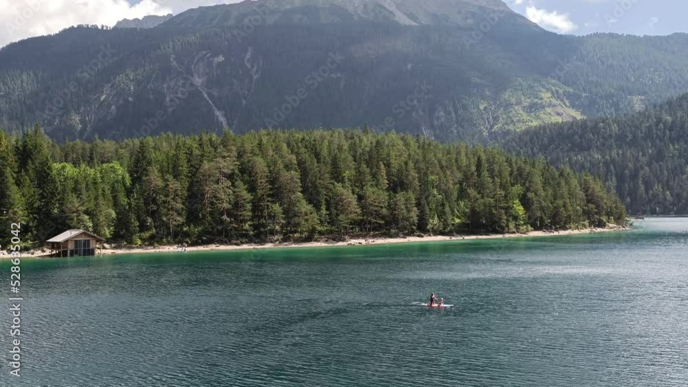 People Stand up Paddle board on a Lake Blindsee in the Mountains in Austria Tyrol, Hut by the Lake in background People Stand up Paddle board on a Lake Blindsee in the Mountains in Austria Tyrol, Hut by the Lake in background