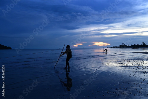 two fishermen are pulling their nets to land from the blue sea