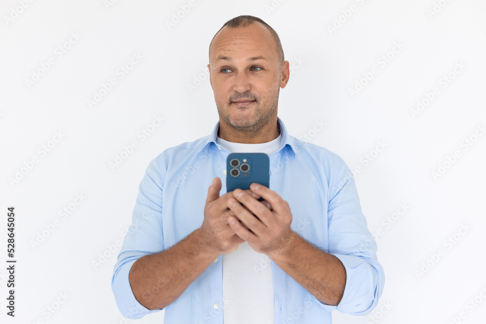 Portrait of smiling mature man texting message on mobile phone. Balding Caucasian guy wearing white T-shirt and blue shirt using smartphone. Mobile communication concept Portrait of smiling mature man texting message on mobile phone. Balding Caucasian guy wearing white T-shirt and blue shirt using smartphone. Mobile communication concept