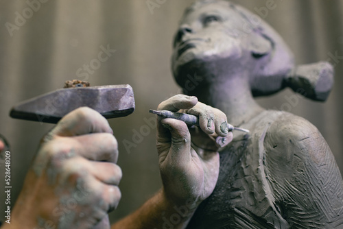 Fototapeta Man sculptor creates sculpt bust human woman sculpture with hammer
