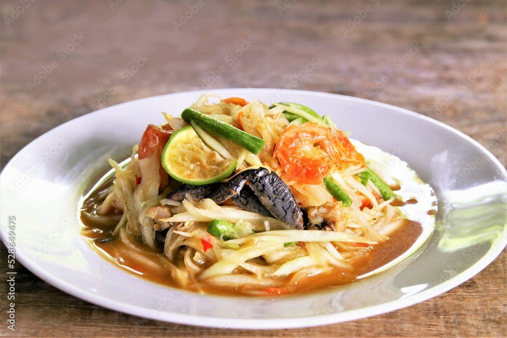 Famous Thai food papaya salad with dried shrimp and salted crab on white plate photo on wooden back ground Famous Thai food papaya salad with dried shrimp and salted crab on white plate photo on wooden back ground