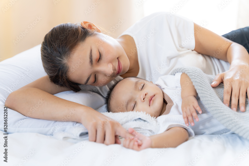 Mom and Newborn,Happy family concept.Close up view of beautiful Asian mother and her sleeping newborn baby.Mother holding baby hand in one hand and holding hand the baby with eyes closing and smiling. Mom and Newborn,Happy family concept.Close up view of beautiful Asian mother and her sleeping newborn baby.Mother holding baby hand in one hand and holding hand the baby with eyes closing and smiling.