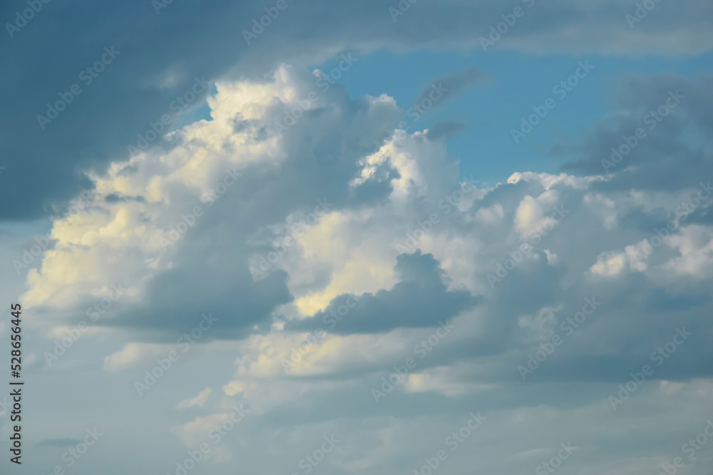 Picturesque sky with thunderstorms cumulus clouds at sunset. Blue sky with big clouds, backlit by sun. Air clouds background. Copy space. Selective focus.