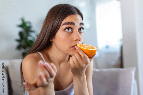 Sick woman trying to sense smell of half fresh orange, has symptoms of Covid-19, corona virus infection - loss of smell and taste. One of the main signs of the disease. photo