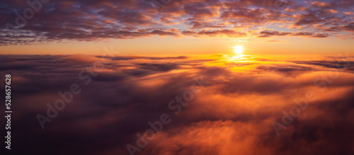 Wide panorama of clouds with setting sun on the background. Aerial drone photo high above the clouds