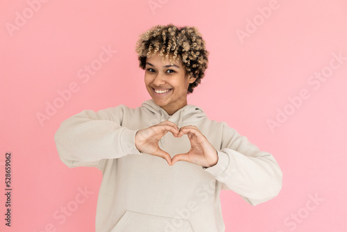 Attractive African American woman making finger heart in studio. Female model with curly hair gesturing. Portrait, studio shot concept