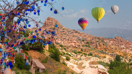 Hot air balloon flying over Cappadocia - Nazars (evil eye) hanging on a tree in Pigeon Valley with Uchisar castle - Cappadocia Turkey