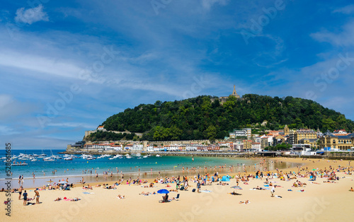 Landscape of La Concha beach in the city of San Sebastian, in the Spanish Basque Country, on a sunny day with people enjoying the beach and Mount Urgull in the background.