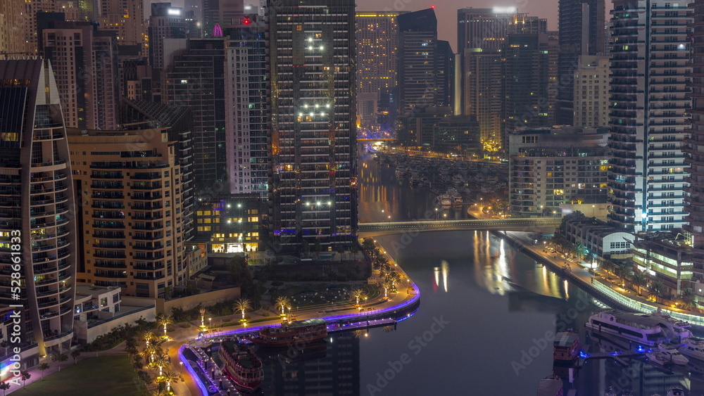 Obraz premium Dubai Marina with several boats and yachts parked in harbor and skyscrapers around canal aerial night to day timelapse.