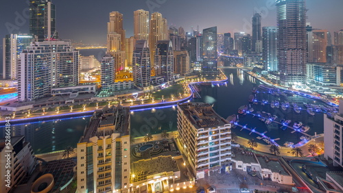 Dubai Marina with several boats and yachts parked in harbor and skyscrapers around canal aerial night to day timelapse.