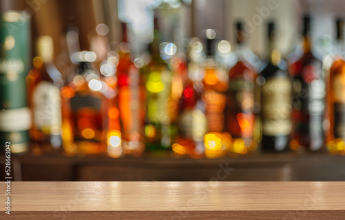 Wooden table top and beautiful bokeh shelves with alcohol bottles at the pub background. Bar concept.