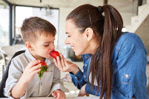 Mother feeds her little son with a strawberry photo