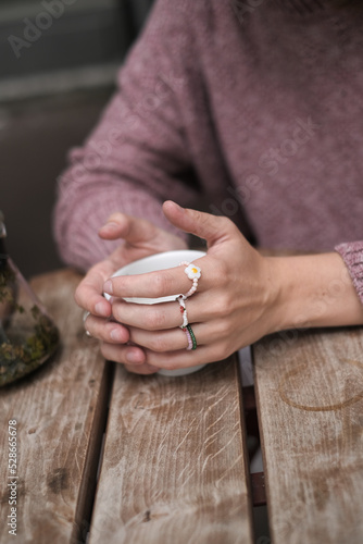Woman's hands holding a cap of tea wearing cute rings sitting on the terrasse in the caffe. Warm autumn vibe