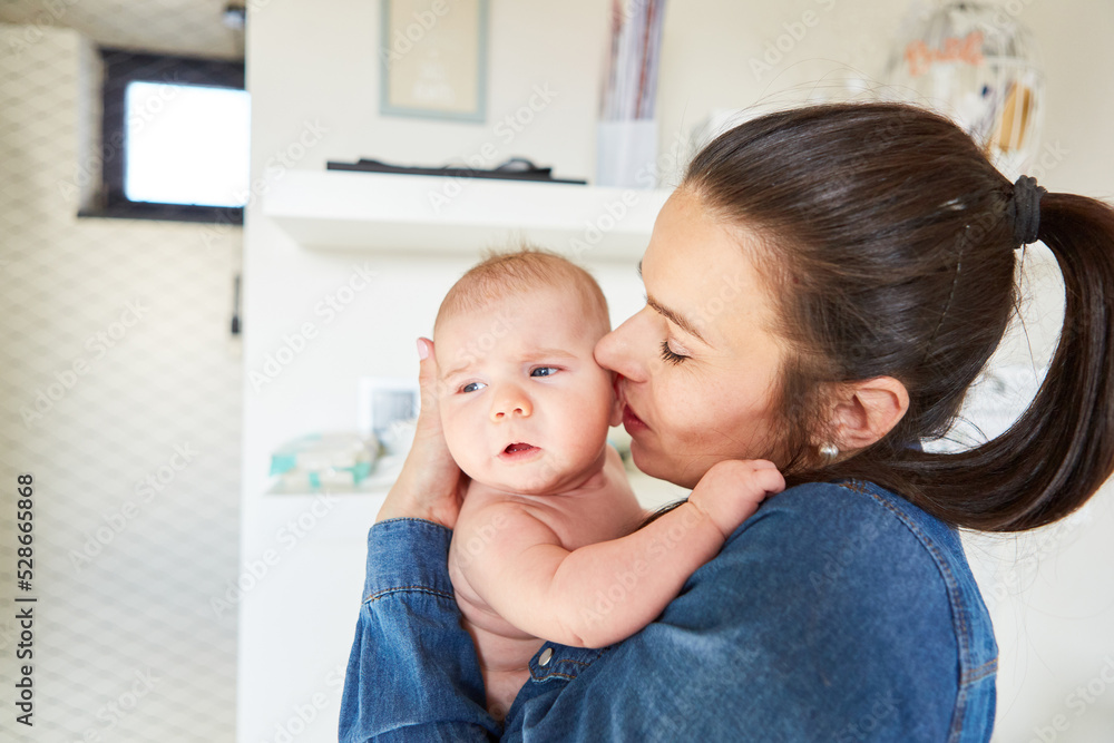 Mother gives baby a tender kiss on the cheek Mother gives baby a tender kiss on the cheek