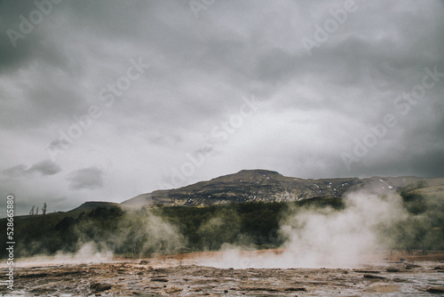 Geyser pool steaming in front of mountain on overcast day