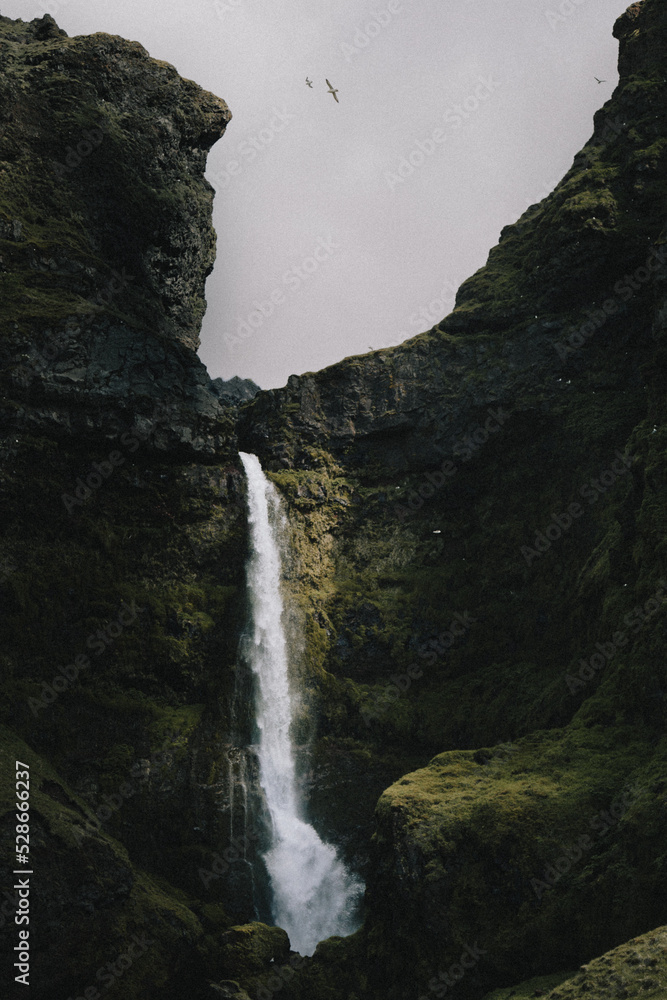 Small waterfall with beam of sunlight set back amongst rocky cliffs