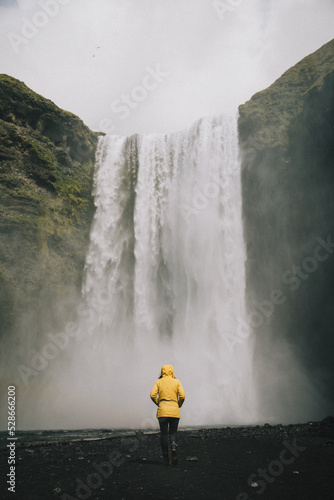 Woman in bright yellow coat standing in front of Skogafoss waterfall