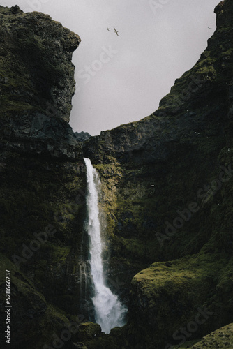 Small waterfall with beam of sunlight set back amongst rocky cliffs