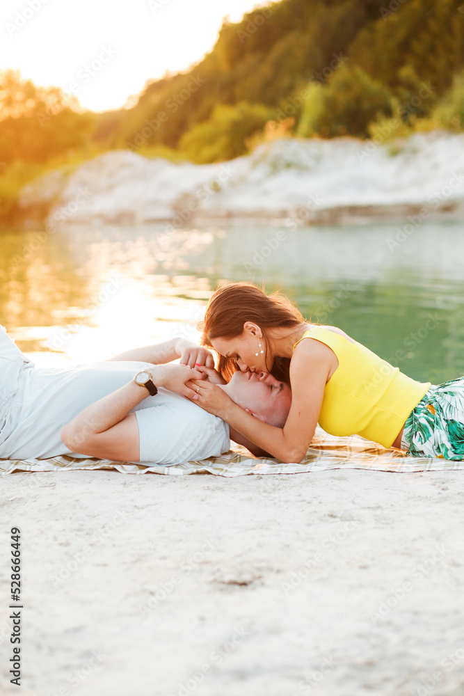 Romantic young couple enjoys a wonderful sunny day having a rest on a blanket by the lake. Love concept.