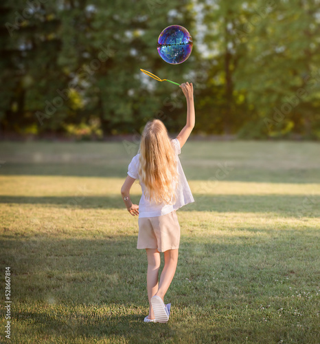The girl stands with her back and blows soap bubbles.