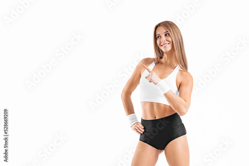 Isolated fit girl pointing at the white wall with copy space. Athlete woman. Muscular young fitness female.