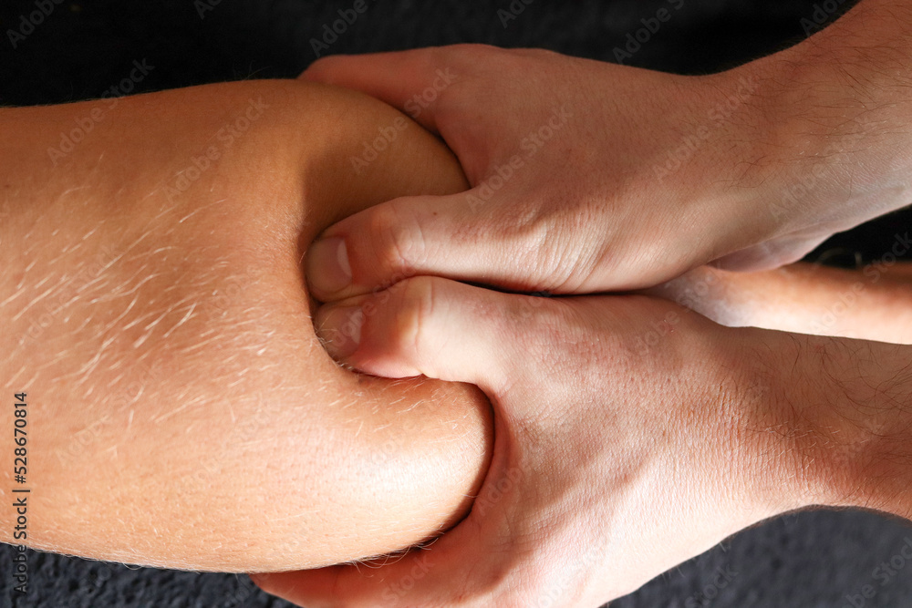 Masseur does legs massage in spa center on gray concrete background. Massage of myofascial trigger points on leg of male client to release tension. Rehabilitation, sport therapy medicine. Masseur does legs massage in spa center on gray concrete background. Massage of myofascial trigger points on leg of male client to release tension. Rehabilitation, sport therapy medicine.
