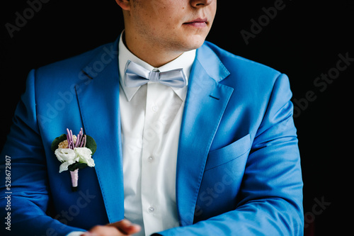 Wedding. The groom in a shirt, bow-tie and a suit with a buttonhole on black wall background. Rich man at wedding day. Close up.