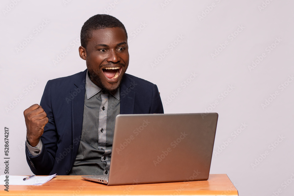 african businessman rejoices while looking at his laptop african businessman rejoices while looking at his laptop