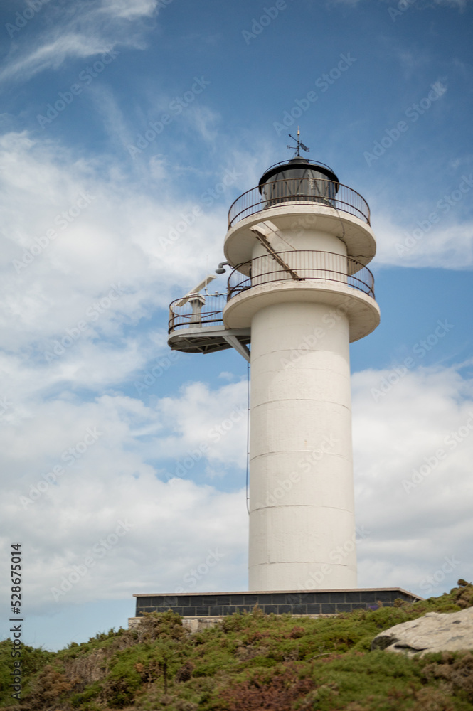 A white lighthouse on top of a hill with a blue sky with clouds