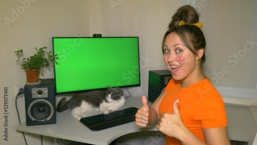 Girl is very happy with what is shown on the computer screen showing thumbs up. Chromakey on computer screen. Cat lies under the screen. Video with a chroma key on the screen to insert any video.