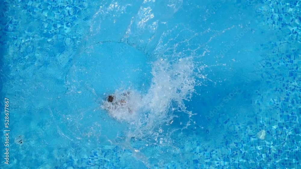 Top view of young woman jumping in pool and splashing crystal clear water. Unrecognizable girl resting and having fun on resort. Lady relaxing during summer vacation or holiday. Slow motion Close up