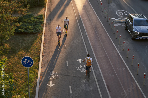 Top aerial view of cyclist and two mans are riding on kick scooters on cycling road. photo