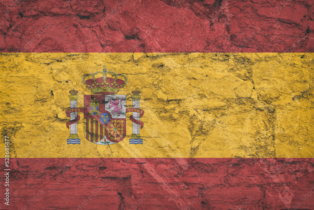 The national flag of Spain on stone wall, grunge background. Spanish flag depicted in bright paint colors on old relief plastering wall