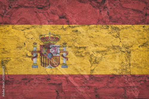 The national flag of Spain on stone wall, grunge background. Spanish flag depicted in bright paint colors on old relief plastering wall