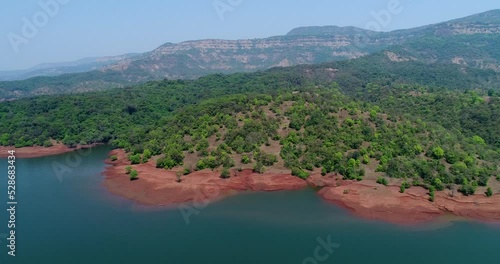 Aerial shot of river running along forest with reddish soil, hill background photo