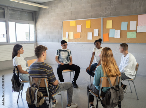 Group of multi-ethnic students sitting in a circle in a classroom while talking about their emotions. Emotional education, assembly, high school