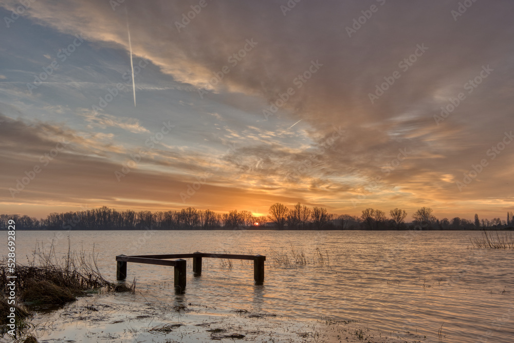 Horizontal view on a wooden railing in high water during sunrise in winter. Sun and clouds in golden hour, landscape with copy space
