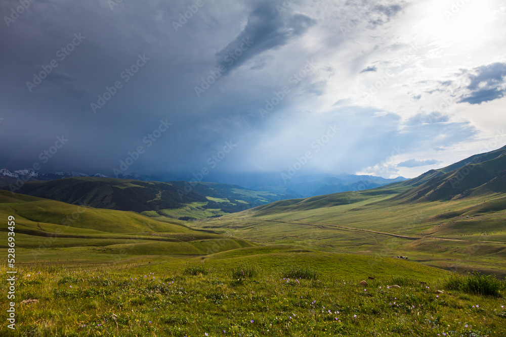 Endless pastures in the valley of the Assy plateau under thunderclouds with the sun
