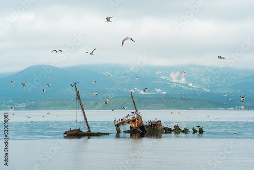 Fotografie shipwreck against the backdrop of a sea bay with foggy mountains in the backgrou