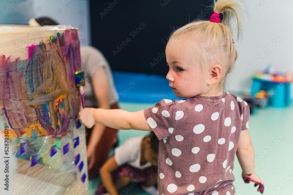 Cling film painting. Little caucasian girl toddler painting with her