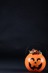 Halloween pumpkin shaped bucket full of candies against black background