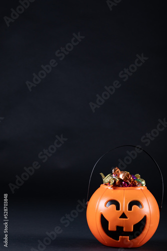 Halloween pumpkin shaped bucket full of candies against black background