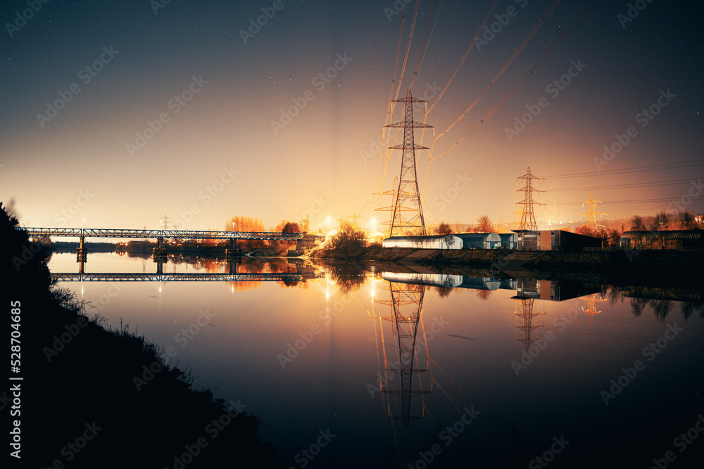 Newburn UK: 6th march 2022: Newburn Bridge Riverside at night electric pylons, rowing club and still river with warm glowing industrial light