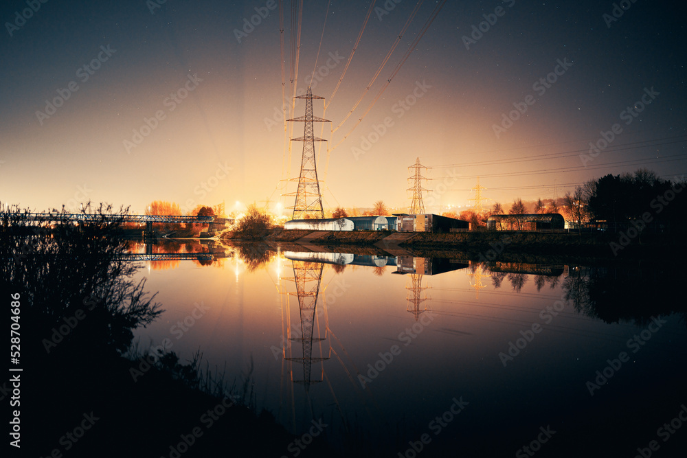 Newburn UK: 6th march 2022: Newburn Bridge Riverside at night electric pylons, rowing club and still river with warm glowing industrial light Newburn UK: 6th march 2022: Newburn Bridge Riverside at night electric pylons, rowing club and still river with warm glowing industrial light