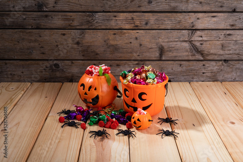 Pumpkin shaped bucket full of halloween candies and toys on wooden surface