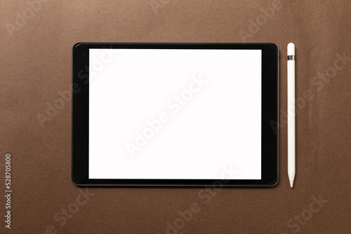 Black tablet with white blank screen is on top of brown paper with supplies. Top view, flat lay.