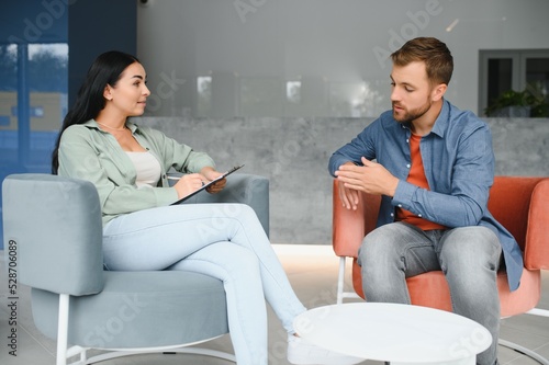 Psychologist talking with patient on therapy session. Depressed man speaking to a therapist while she is taking notes.