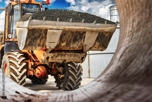 A large front loader transports crushed stone or gravel in a bucket at a construction site or concrete plant. Transportation of bulk materials. Construction equipment. Bulk cargo transportation.